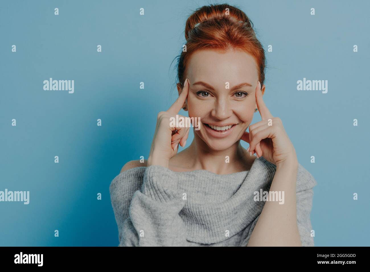 Giovane donna dai capelli rossi positivi con le dita sui templi in piedi isolato su sfondo blu Foto Stock