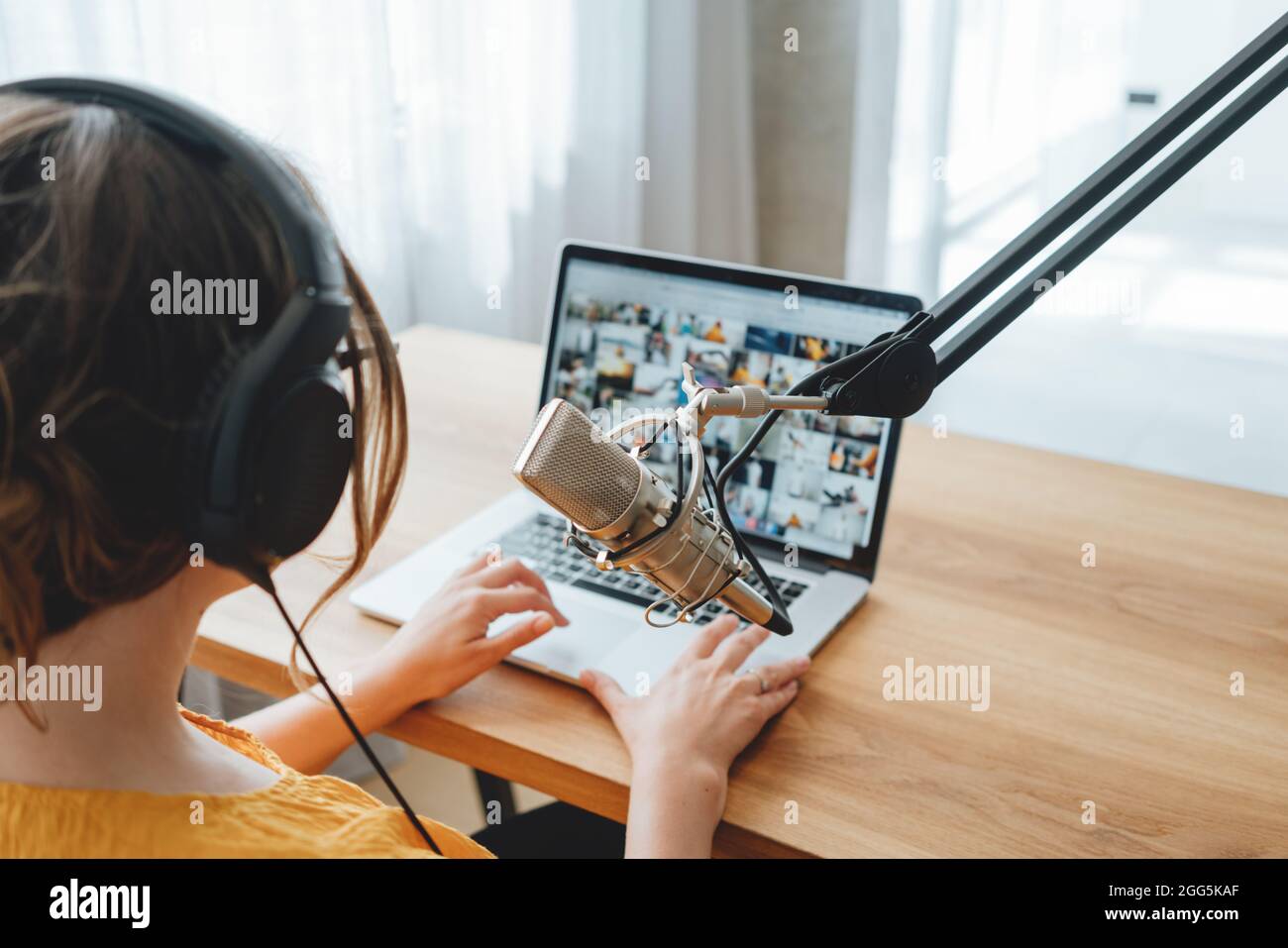 Podcaster femminile che registra il suo podcast utilizzando il microfono e il portatile presso il suo studio di trasmissione a casa. Donna in streaming dal vivo da casa studio radio Foto Stock