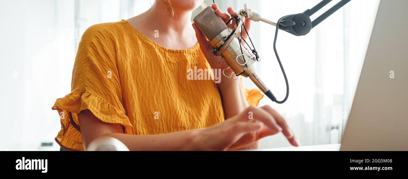 Donna radio ospite di registrare e trasmettere il suo podcast da casa studio. Il podcaster femmina parla nel microfono sul tavolo. Immagine ampia. Primo piano Foto Stock