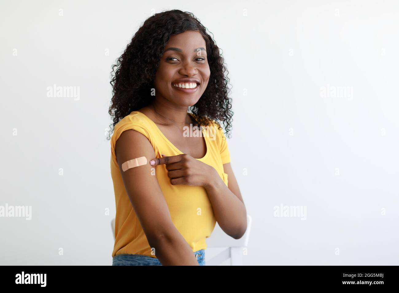 Black Lady che mostra braccio vaccinato dopo l'iniezione del vaccino, sfondo grigio Foto Stock