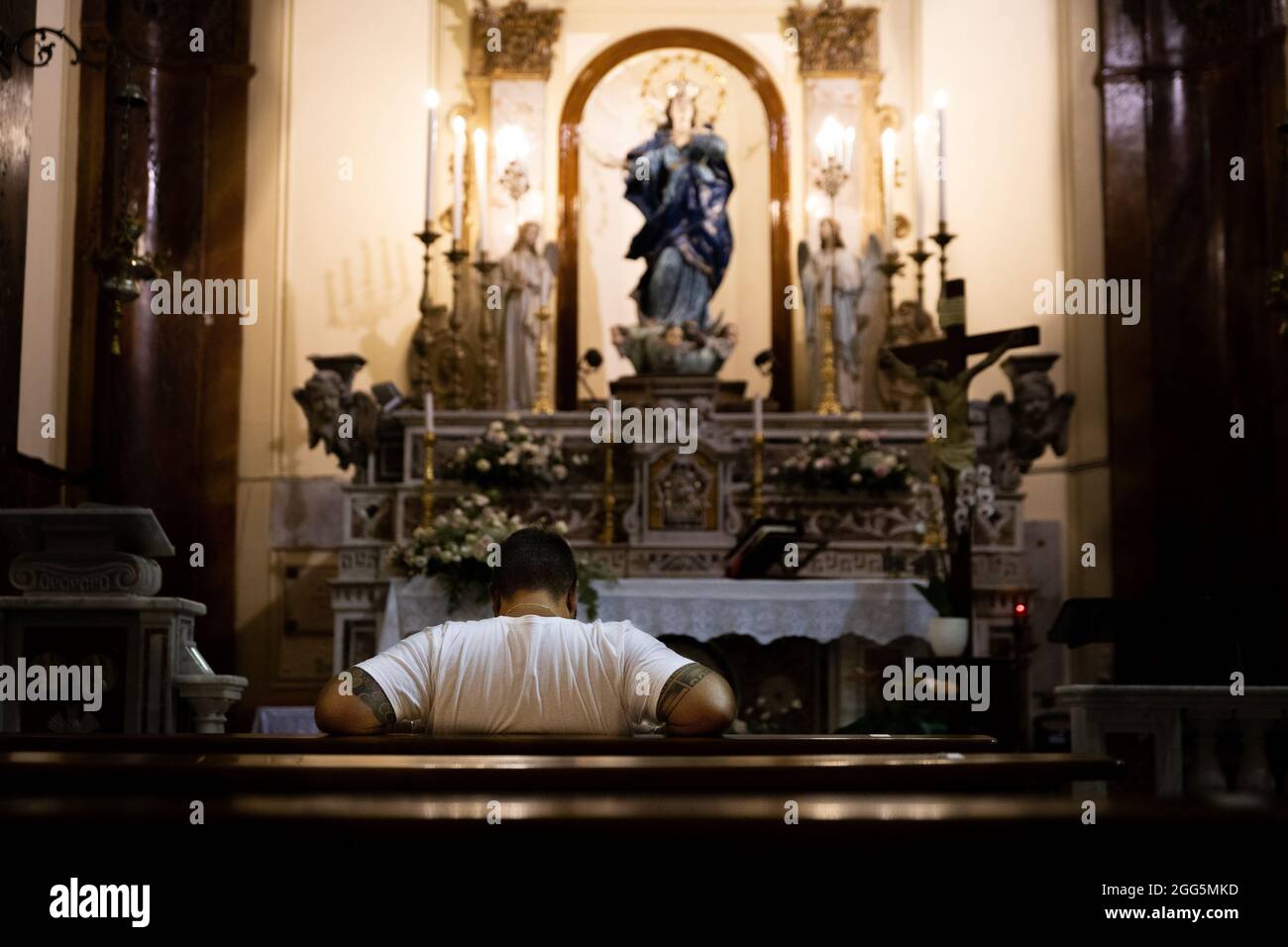 L'uomo prega in una chiesa di fronte alla statua della Vergine maria Foto Stock