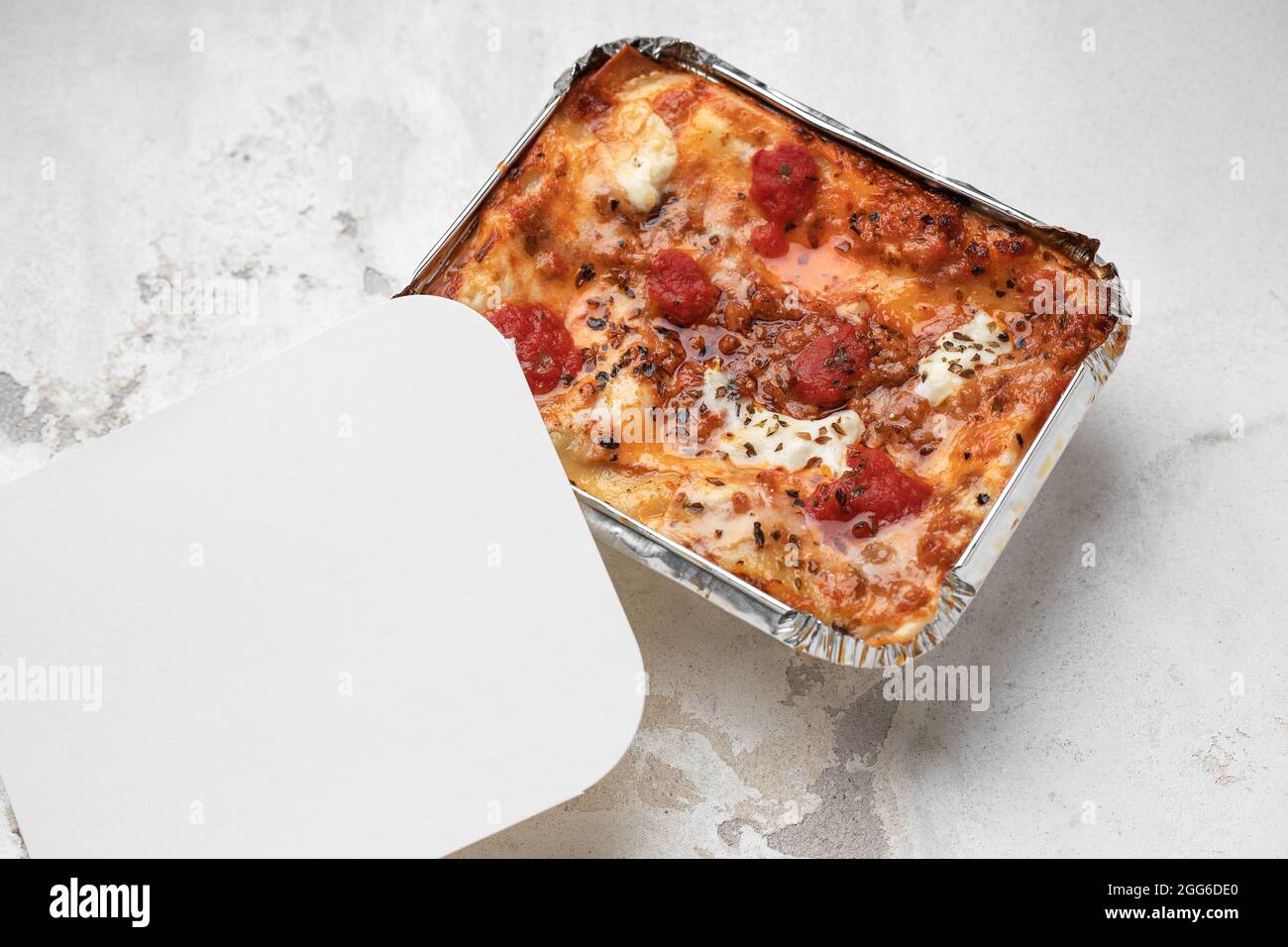 Togliere la lasagna cremosa con mozzarella fresca e pomodori su fondo di argilla bianca Foto Stock