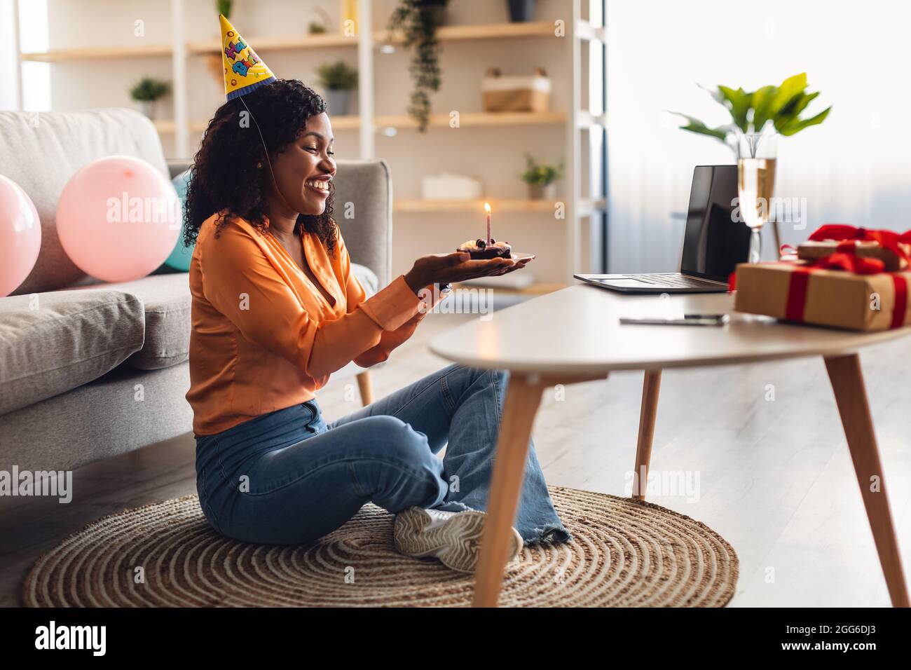 African American Female Holding Birthday Cake seduta al laptop Indoor Foto Stock