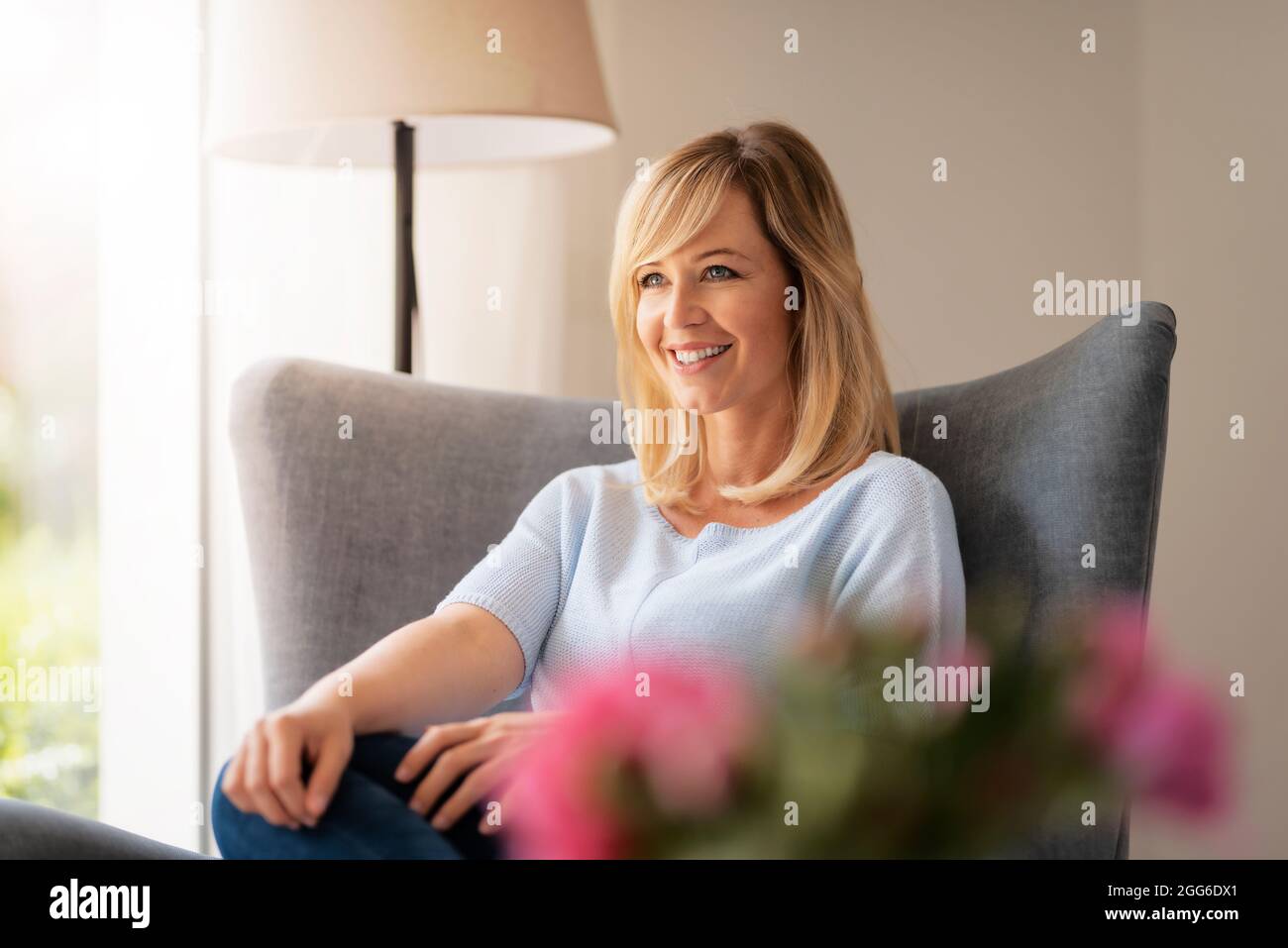 Donna sorridente con capelli biondi che si rilassa alla poltrona a casa. Foto Stock