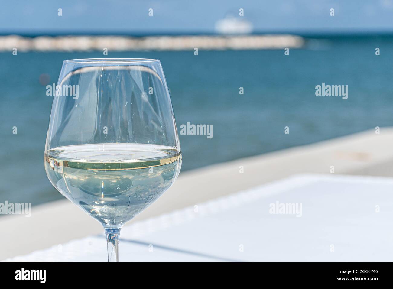 Bicchiere di vino bianco su un tavolo con mare blu e nave sullo sfondo Foto Stock