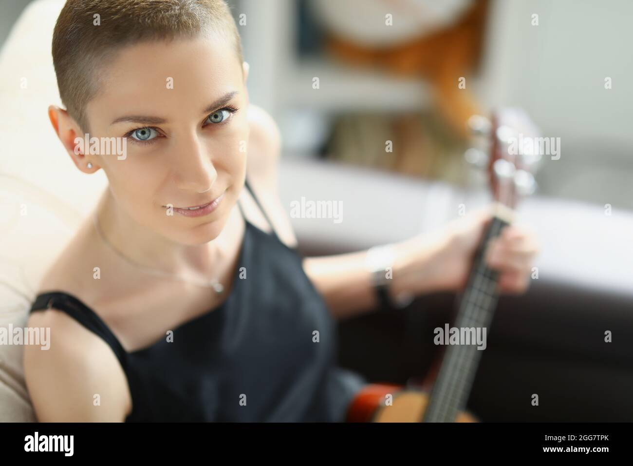 Giovane donna elegante in abito nero che gioca ukulele Foto Stock