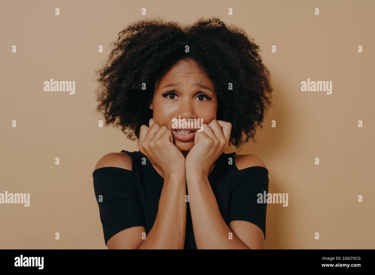 Spaventato razza femminile mista aspetto nervoso e sensazione di stress mentre si posa su sfondo beige Foto Stock