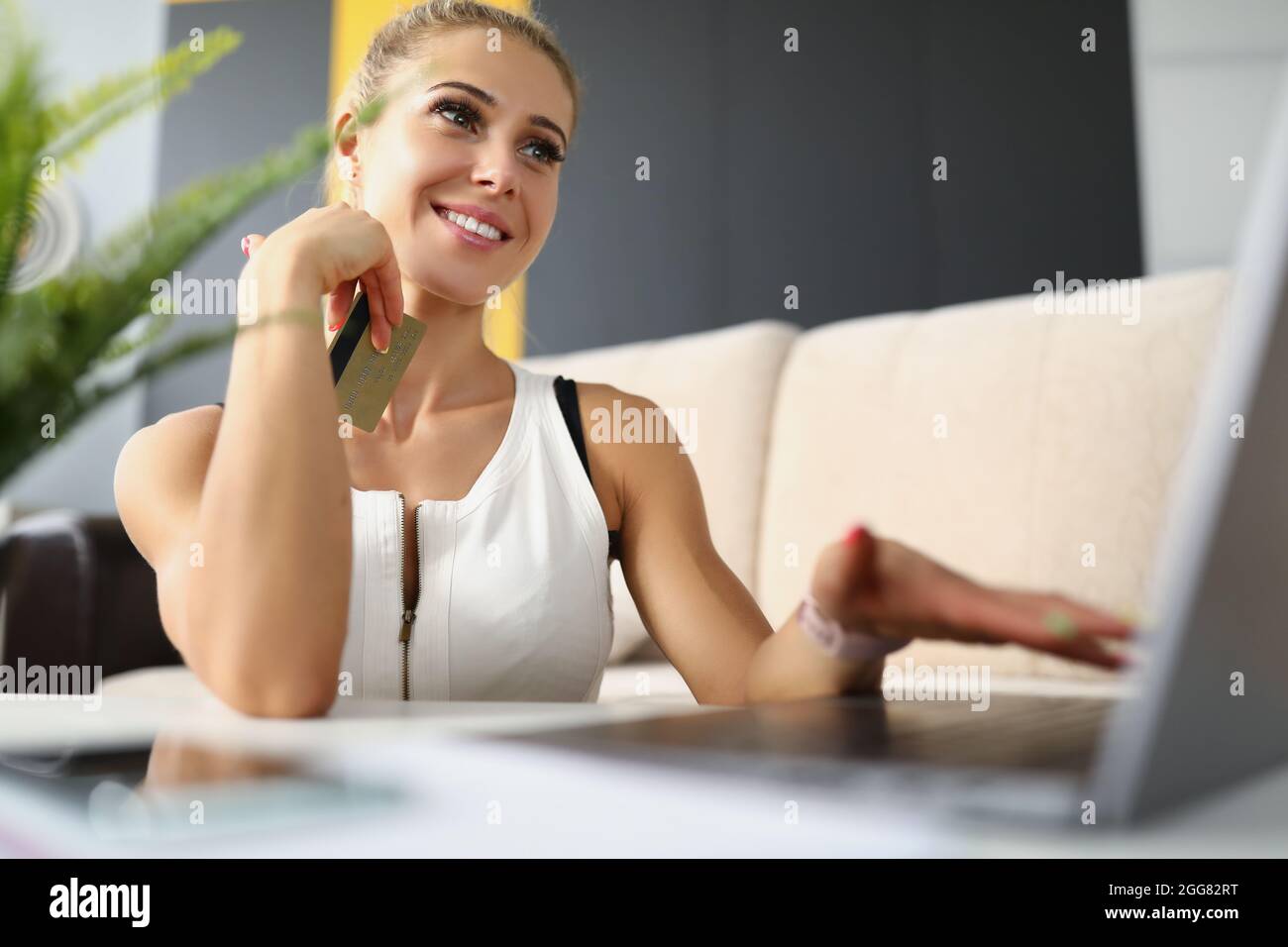 Donna bionda seduta da computer portatile con carta di credito Foto Stock