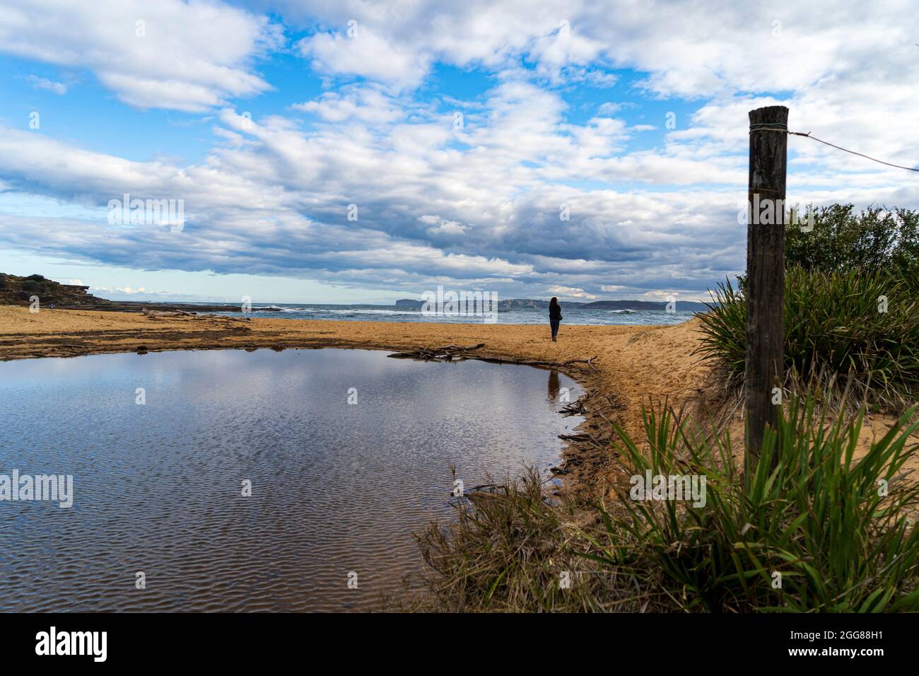 Putty Beach, Central Coast, NSW, Australia in una giornata di tempesta selvaggia guardando attraverso le increspature di una laguna ad una figura solitaria guardando l'oceano Foto Stock