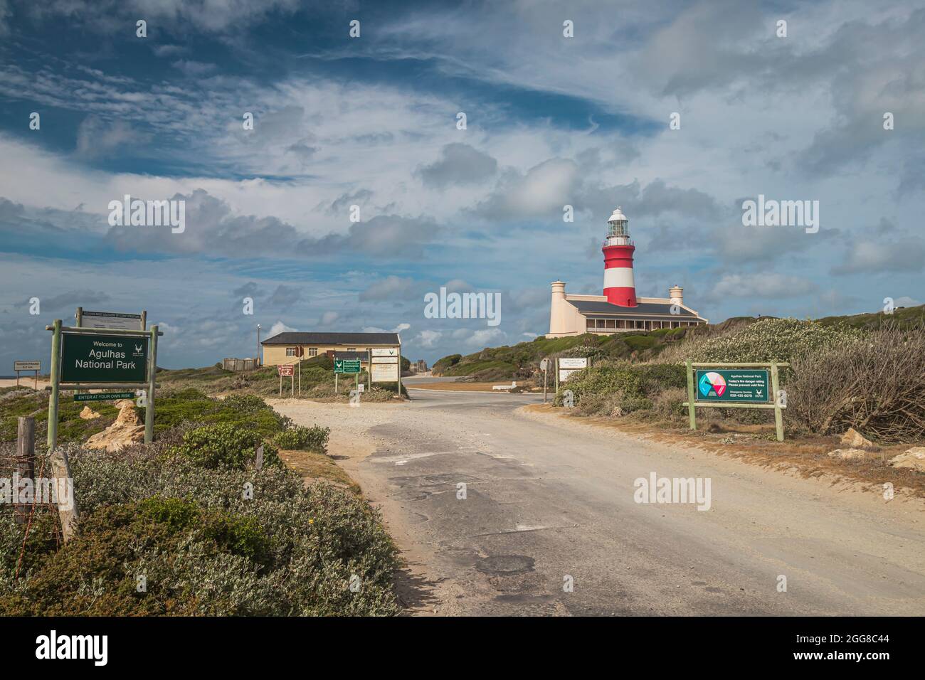 Una strada d'ingresso al Parco Nazionale di Capo Agulhas con il Faro di Capo Agulhas sullo sfondo, che è il punto più meridionale del continente africano. Foto Stock