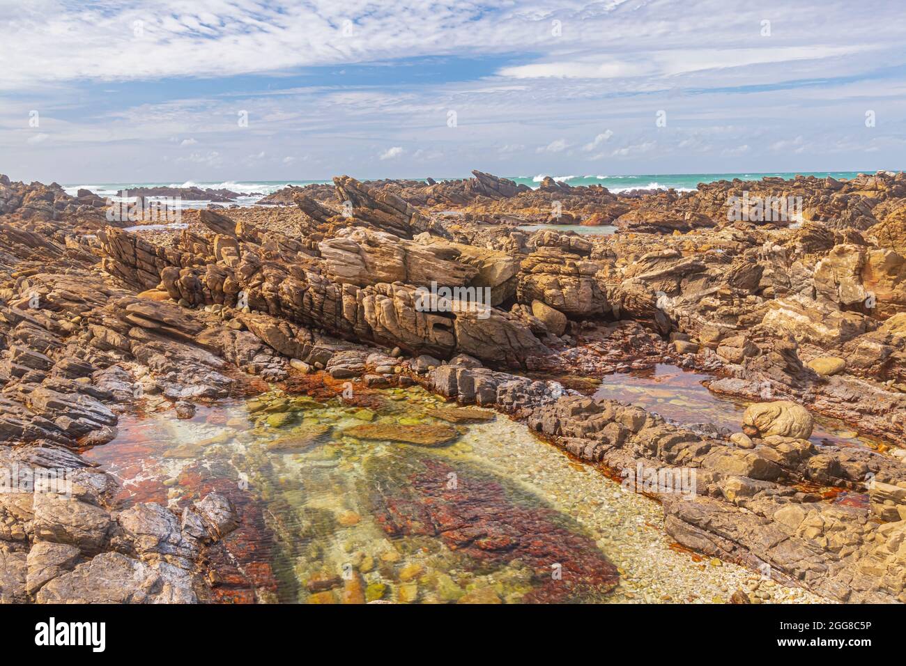 Formazioni rocciose con piscina di marea sulla riva di Capo Agulhas in Sud Africa che è il punto più meridionale del continente africano. Foto Stock