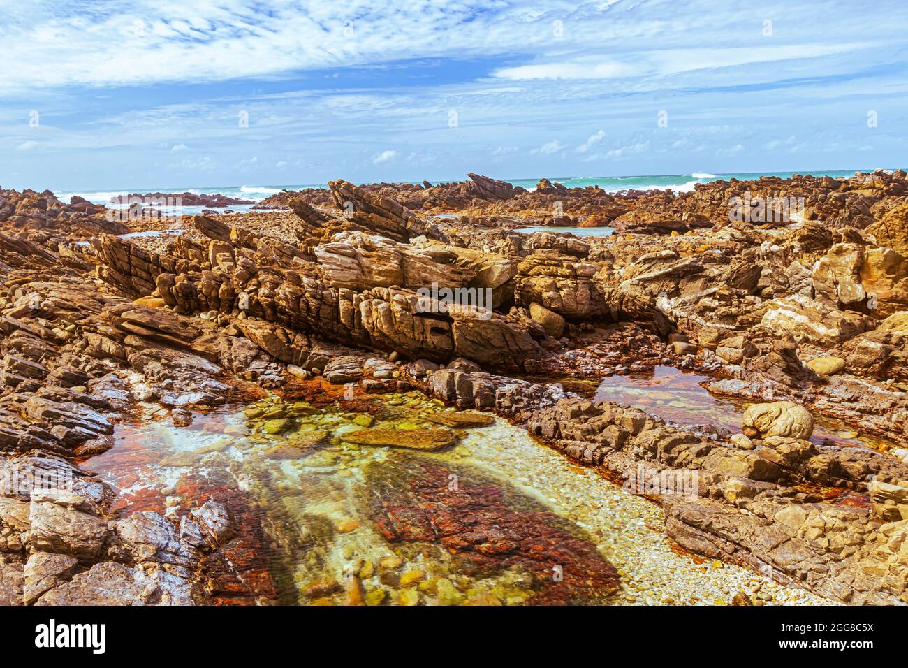 Formazioni rocciose con piscina di marea sulla riva di Capo Agulhas in Sud Africa che è il punto più meridionale del continente africano. Foto Stock