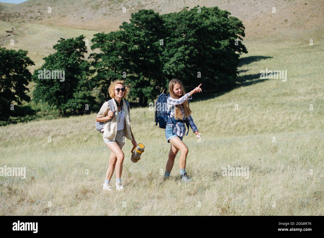 Allegre donne amici escursioni in colline erbose, andando in salita, parlando. Puntando a distanza. Foto Stock