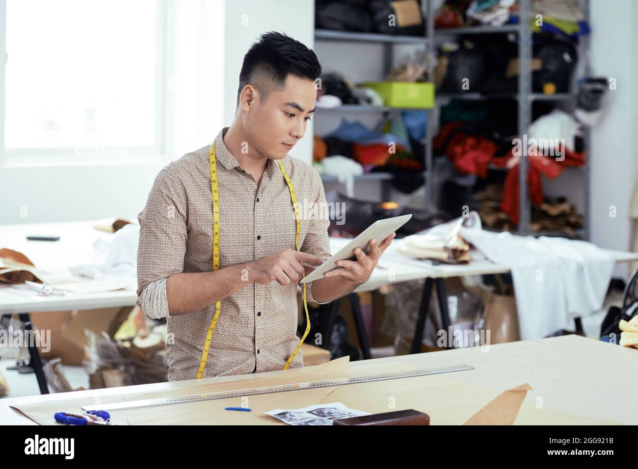 Un lavoratore di produzione di abbigliamento serio che verifica nuovi modelli sul computer tablet Foto Stock