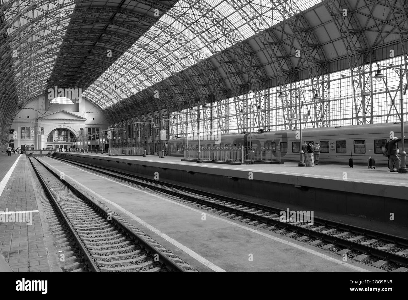 Mosca. Russia. Agosto 29, 2021. Archi a volta che sostengono un grande tetto di vetro che copre le rotaie della stazione ferroviaria e un treno che ferma alla piattaforma. Immagine in bianco e nero. Foto Stock