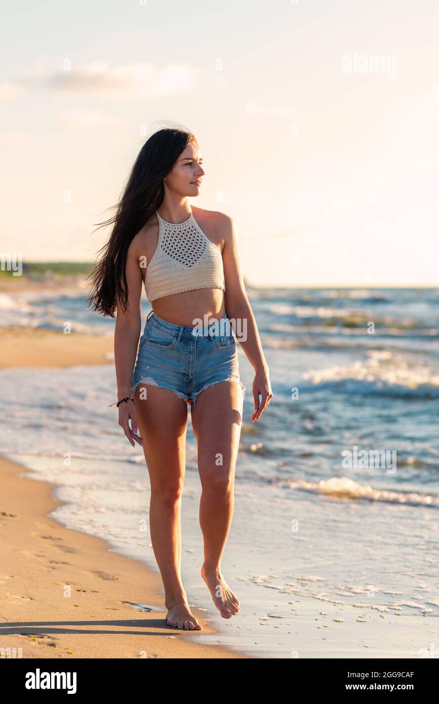 Solitaria giovane donna che cammina sulla spiaggia Sunset day.Beach donna in moda beachwear rilassante camminare vicino all'acqua dell'oceano durante i viaggi estivi di vacanza. Foto Stock