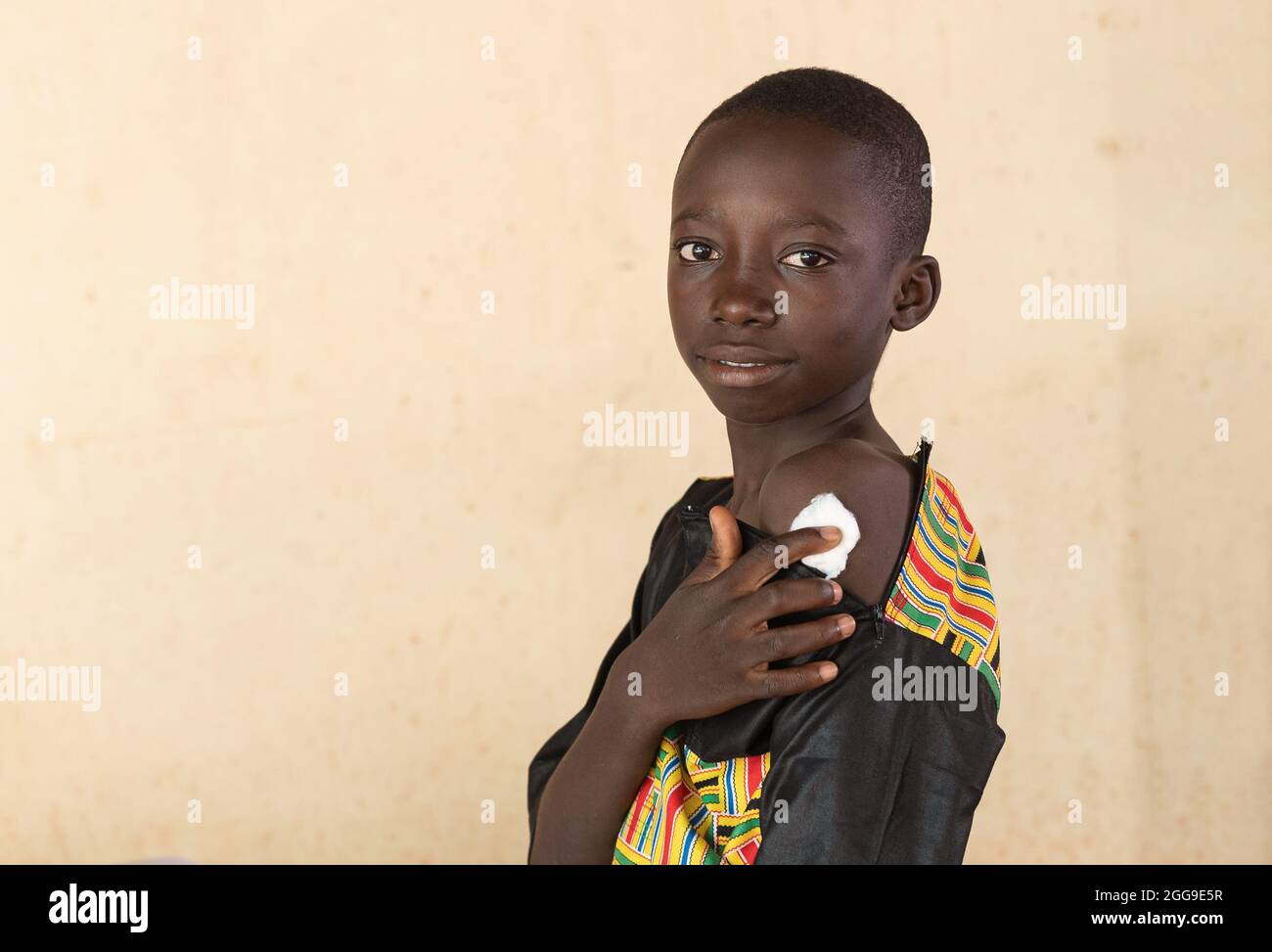 Giovane ragazzo africano nero astuto che preme un batuffolo di cotone disinfettante sul sito di iniezione sul braccio sinistro; concetto di vaccinazione di Covid-19 Foto Stock