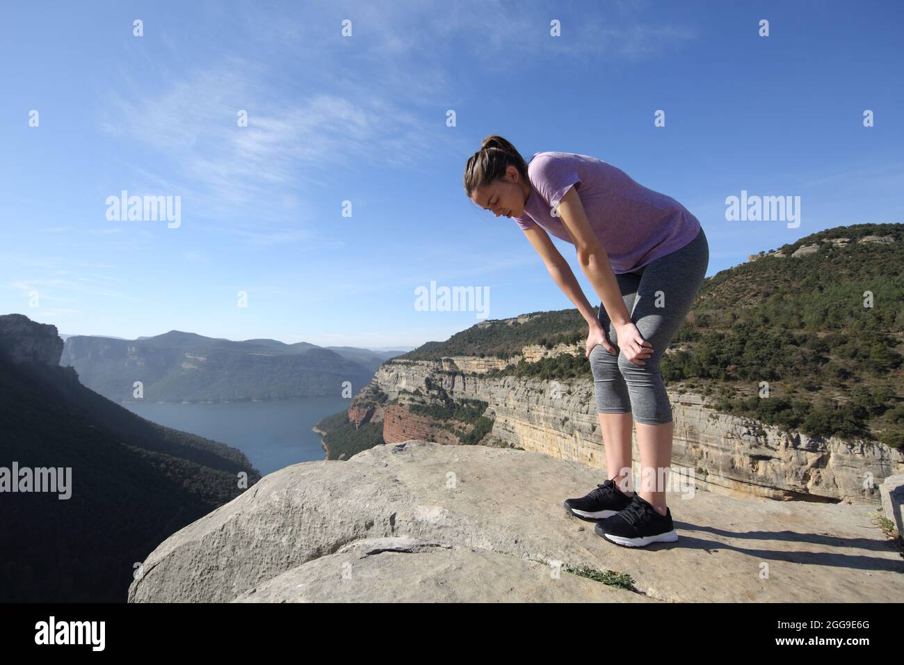 Esausto corridore che riposa dopo lo sport in piedi sulla cima di una scogliera nella montagna Foto Stock