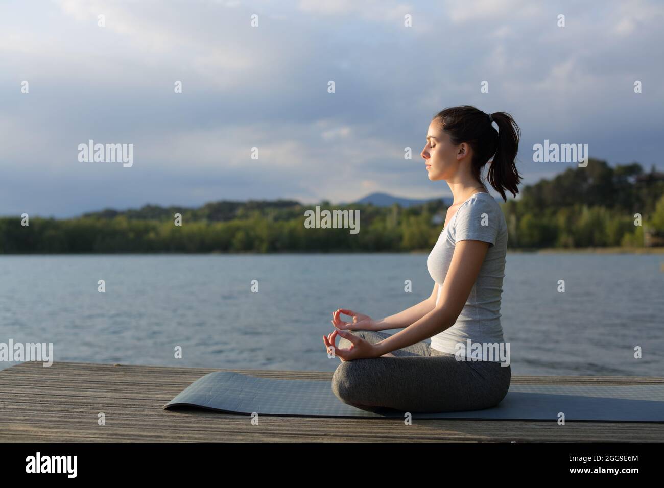 Profilo di una donna rilassata che fa esercizio di yoga in un lago al tramonto Foto Stock