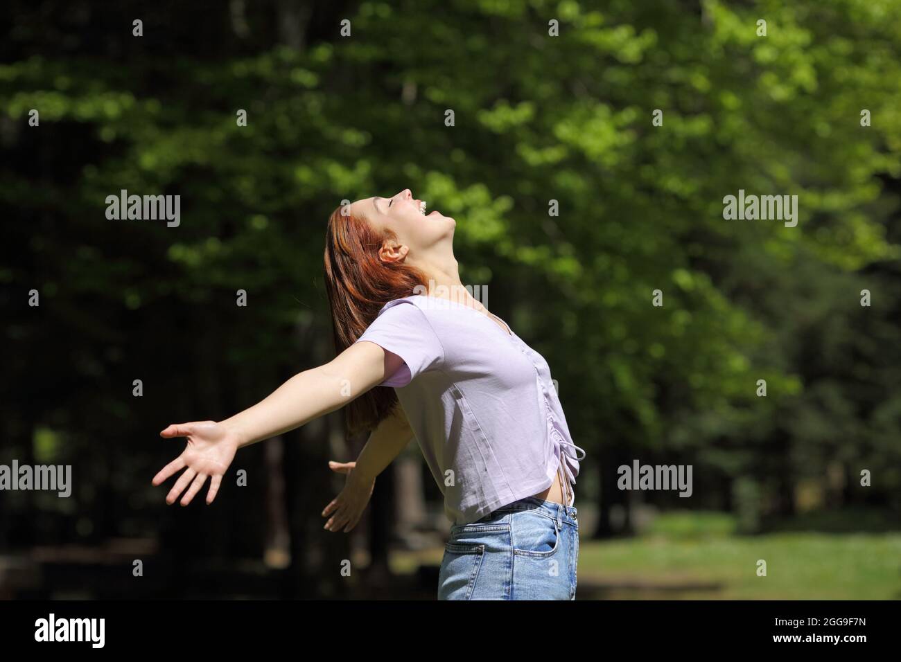 Donna felice urlando per l'aria che stretching braccia in una foresta Foto Stock