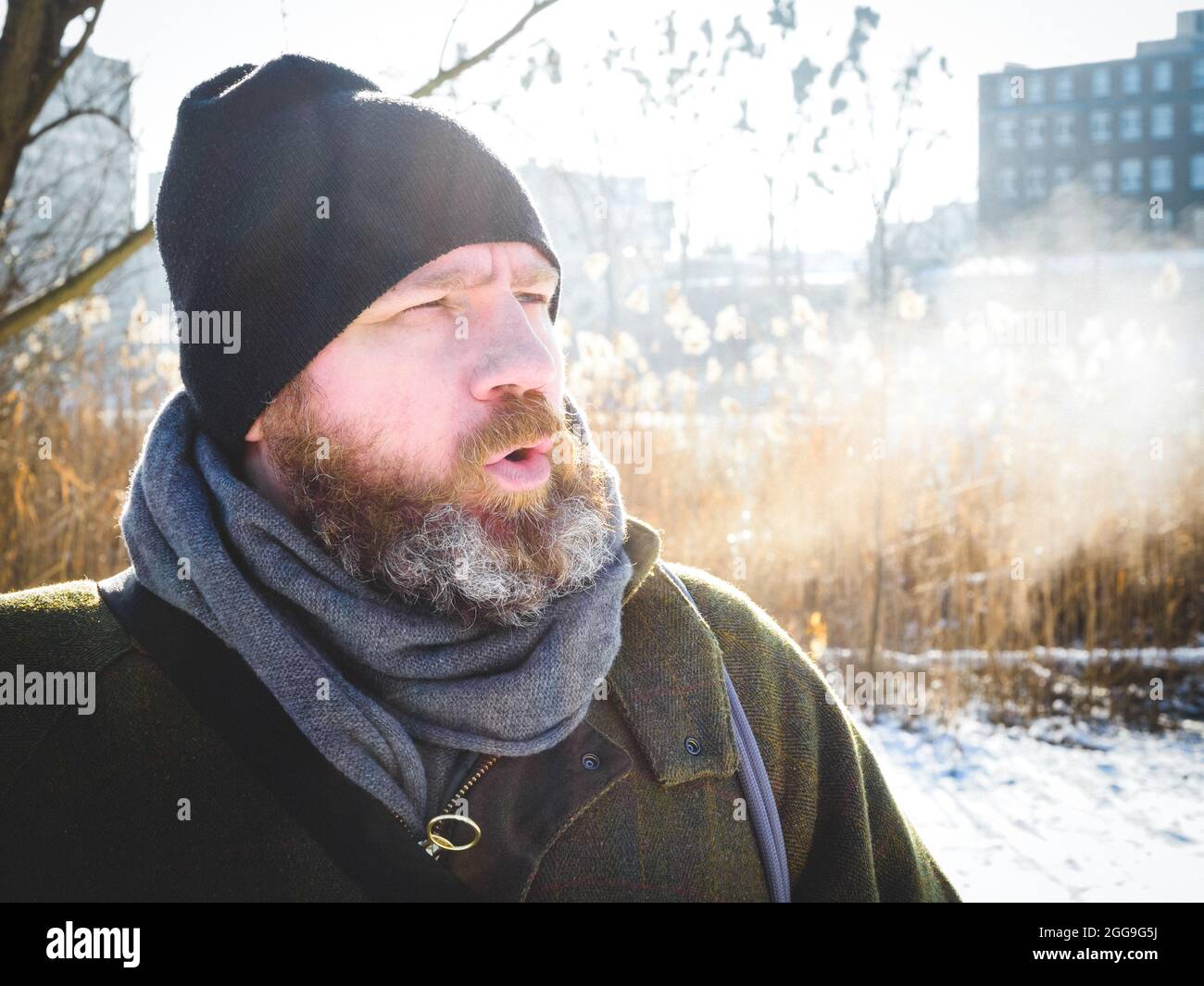 L'uomo respira nella foresta d'inverno. Uomo adulto che indossa un cappello a maglia, respirando aria fredda. Uomo bearded rilassante sulla passeggiata invernale nella foresta innevata, candid cattura, l Foto Stock