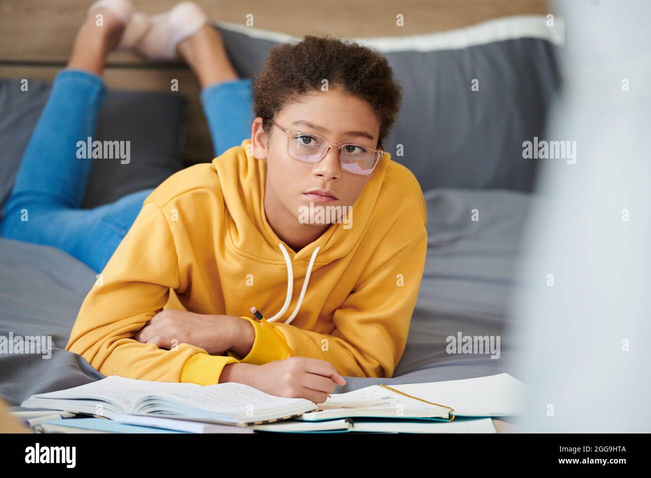 Ragazza adolescente in occhiali sdraiati sul letto e scrivere un saggio in  un libro di testo per la classe inglese Foto stock - Alamy