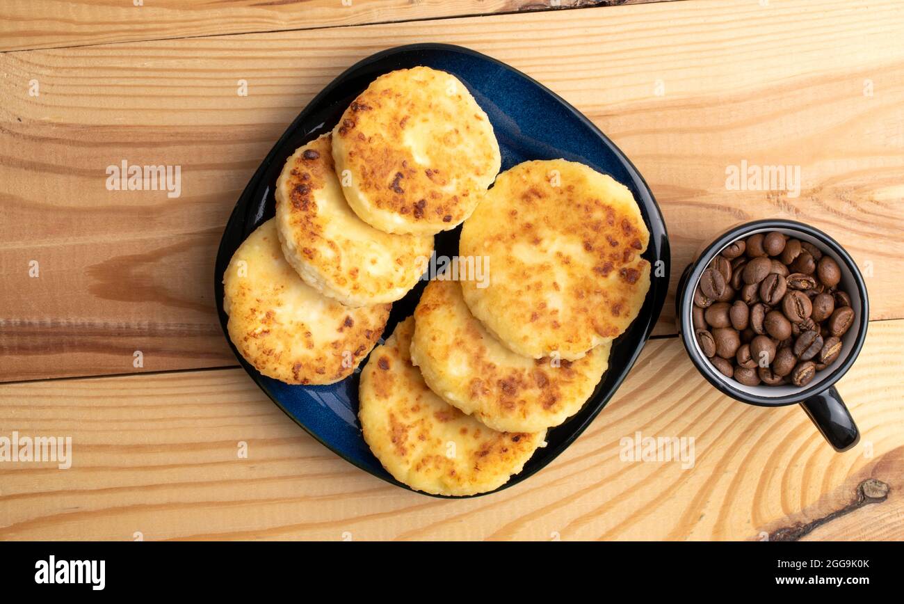 Diverse frittelle fragranti su un piatto di ceramica con una tazza di caffè, primo piano, su un tavolo di legno bianco, vista dall'alto. Foto Stock