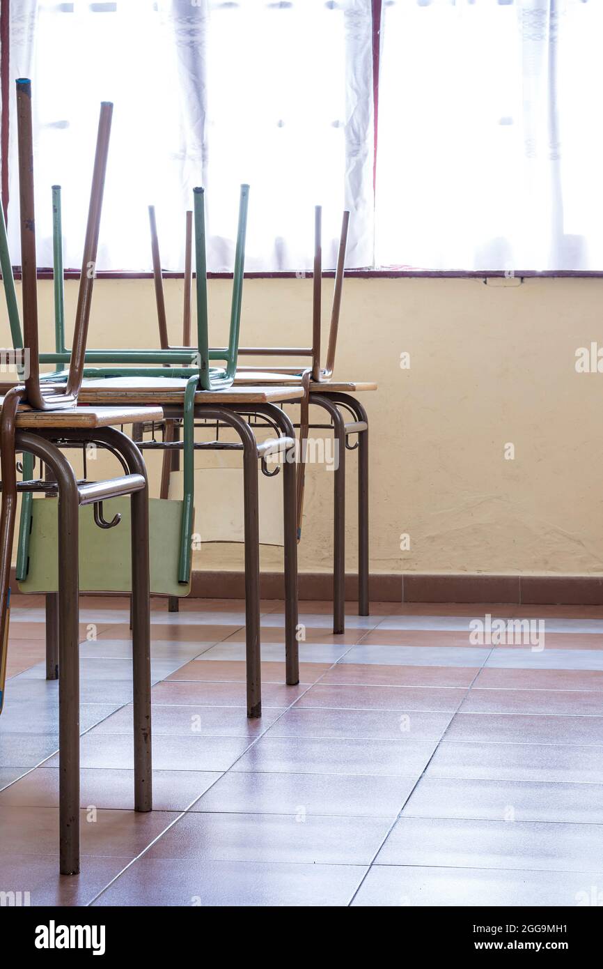 Le sedie della scuola del bambino alzate sulla parte superiore della scrivania.la fotografia è presa in formato ritratto. Foto Stock