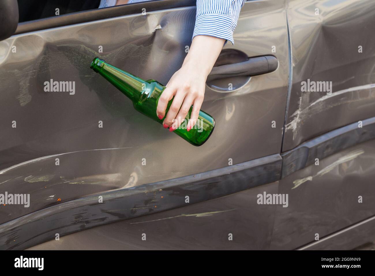 Ritratto senza volto della mano femminile appesa al finestrino dell'auto con bottiglia di bevanda alcolica, guasto dovuto a conducente ubriaco, reati di traffico ubriaco dr Foto Stock