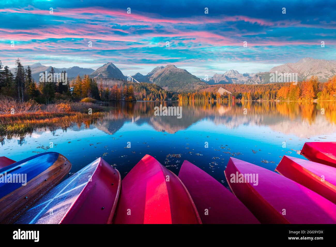 Pittoresca vista autunnale del lago Strbske pleso nel Parco Nazionale di High Tatra, Slovacchia. Fila di barche di legno rosso e alte montagne sullo sfondo. Fotografia di paesaggio Foto Stock