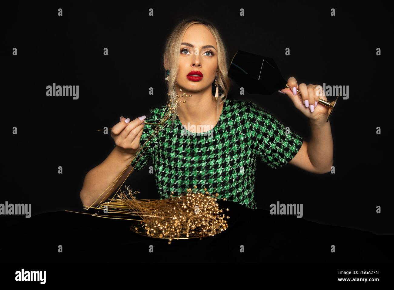 Dieta in oro nuziale per la giovane donna bionda di lusso in abito verde su sfondo nero è annoiato sulla dieta. Concetto di disturbo alimentare. Foto studio. Moda a Foto Stock