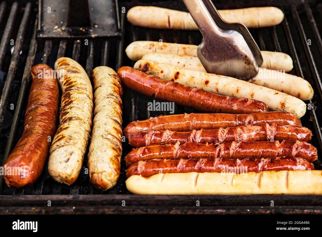 le deliziose salsicce vengono cucinate sulla griglia sopra un fuoco aperto. Festa del cibo in città sulla strada. Le salsicce di Monaco vengono grigliate presso il food Court Foto Stock