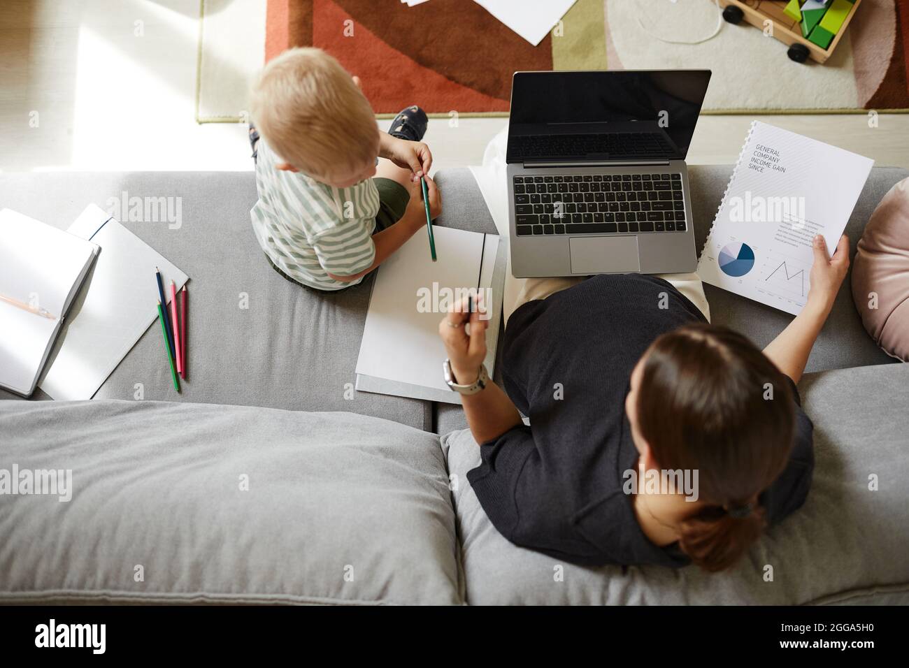 Direttamente sopra la vista della madre incinta seduta con il laptop sulle ginocchia e lavorare con le finanze mentre suo figlio parla con lei Foto Stock