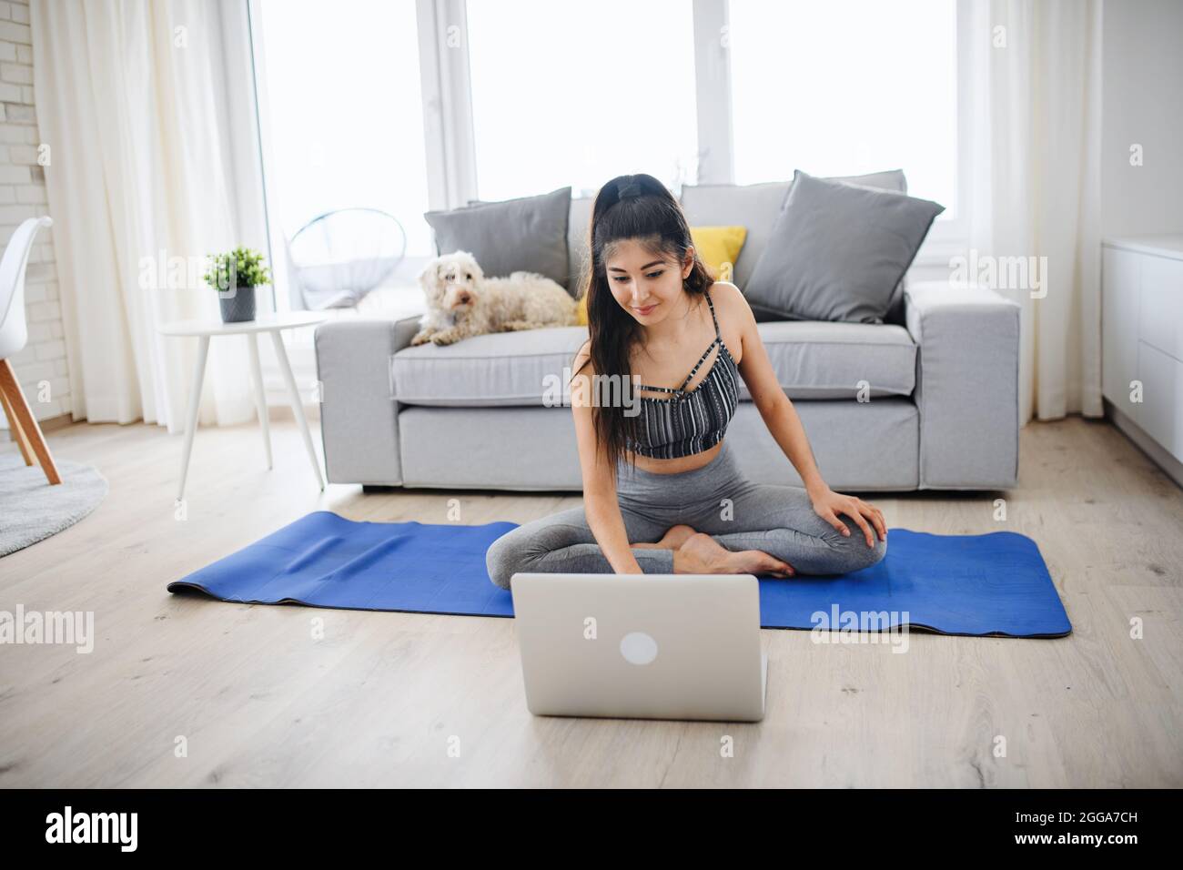 Ritratto di giovane donna sportiva con computer portatile che fa esercizio in casa, sano stile di vita concetto. Foto Stock