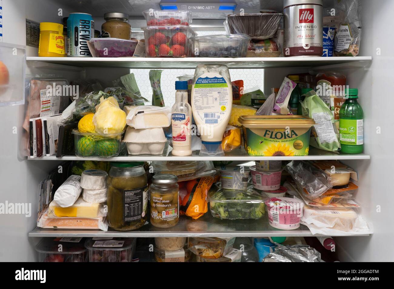 L'interno di un frigorifero britannico con scaffali riempiti con una selezione di frutta fresca e verdure, condimenti, salse, burro, uova e alcol. Foto Stock