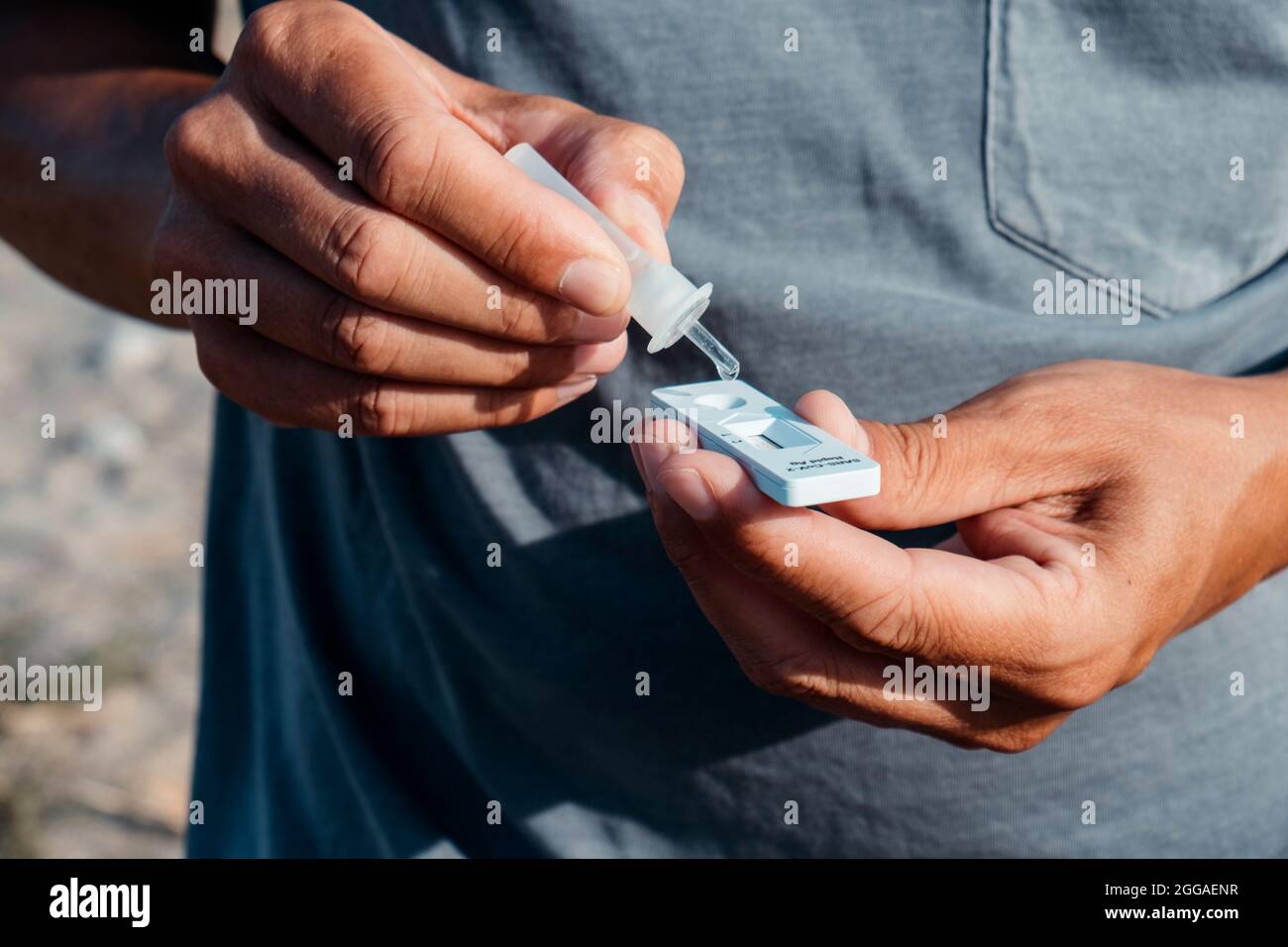 un giovane uomo caucasico all'aperto, indossando una t-shirt casual grigia, inserisce il contenuto di una pipetta con il proprio campione nella diagnosi dell'antigene covid-19 Foto Stock