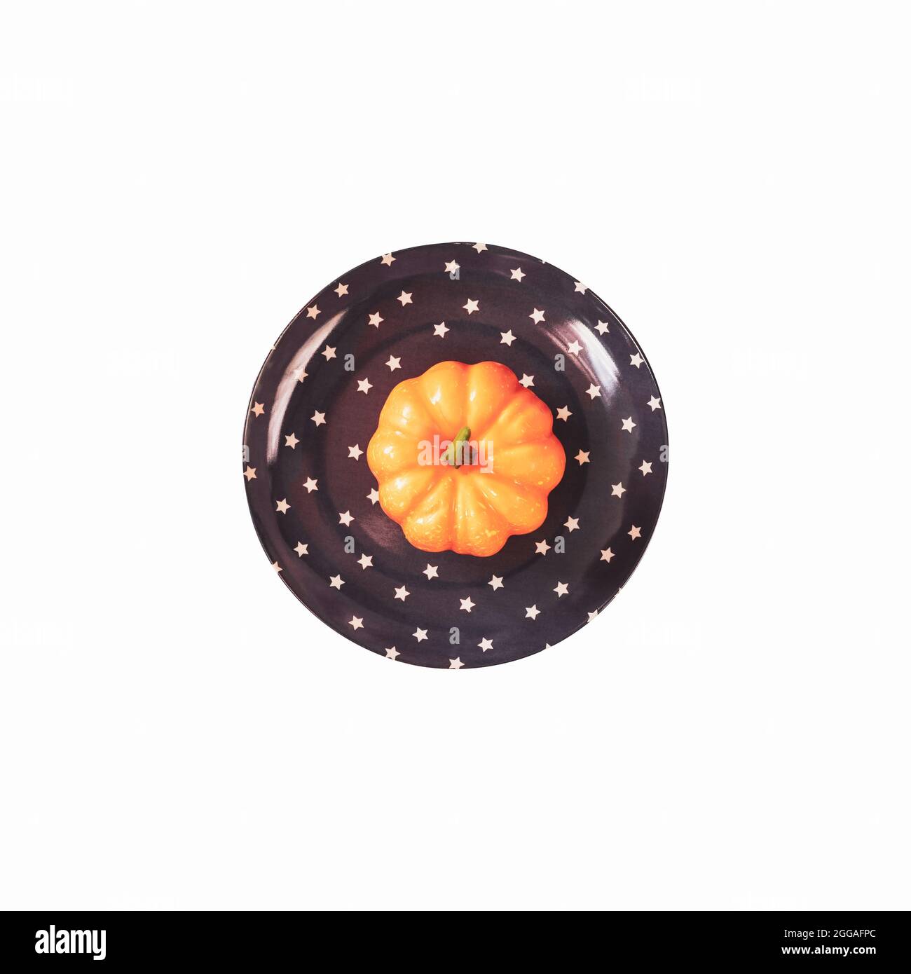 Piccola zucca arancione isolata su un piatto scuro con stelle su sfondo bianco. Un elemento del disegno domestico per Halloween. Giorno di ringraziamento, Halloween p Foto Stock