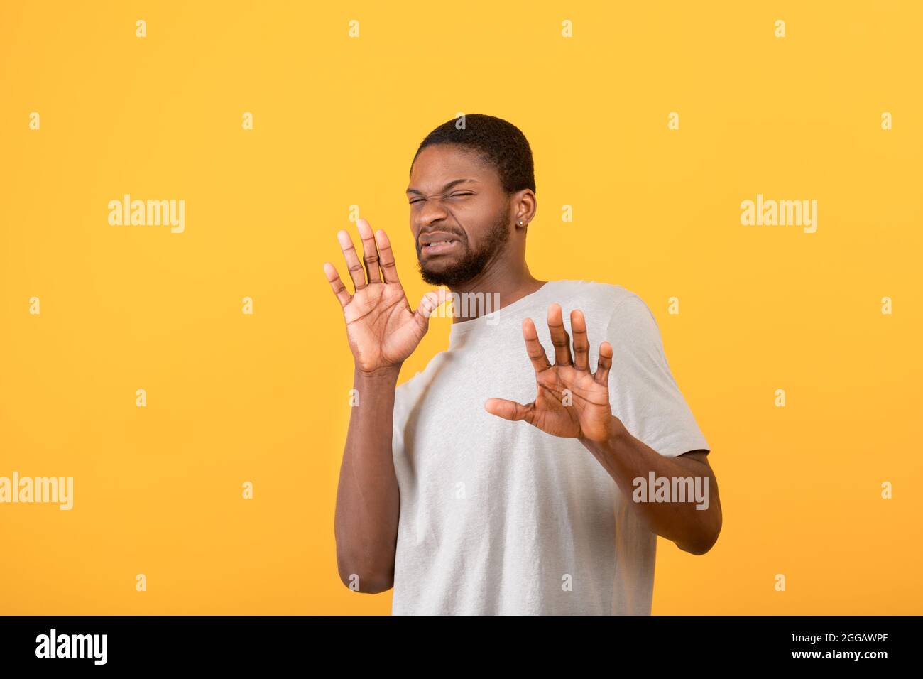 Uomo nero disgustato che mostra STOP gesture con entrambe le mani, esprimendo rifiuto su sfondo giallo studio Foto Stock