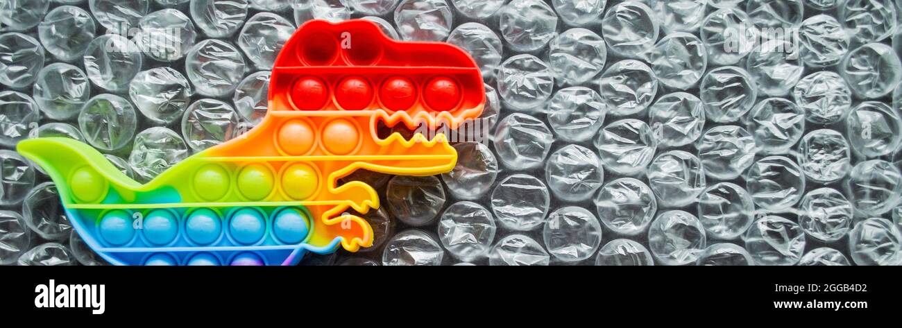 Banner con pop giocattolo è dinosauro arcobaleno colori su uno sfondo bolla. Spazio di copia. Foto Stock