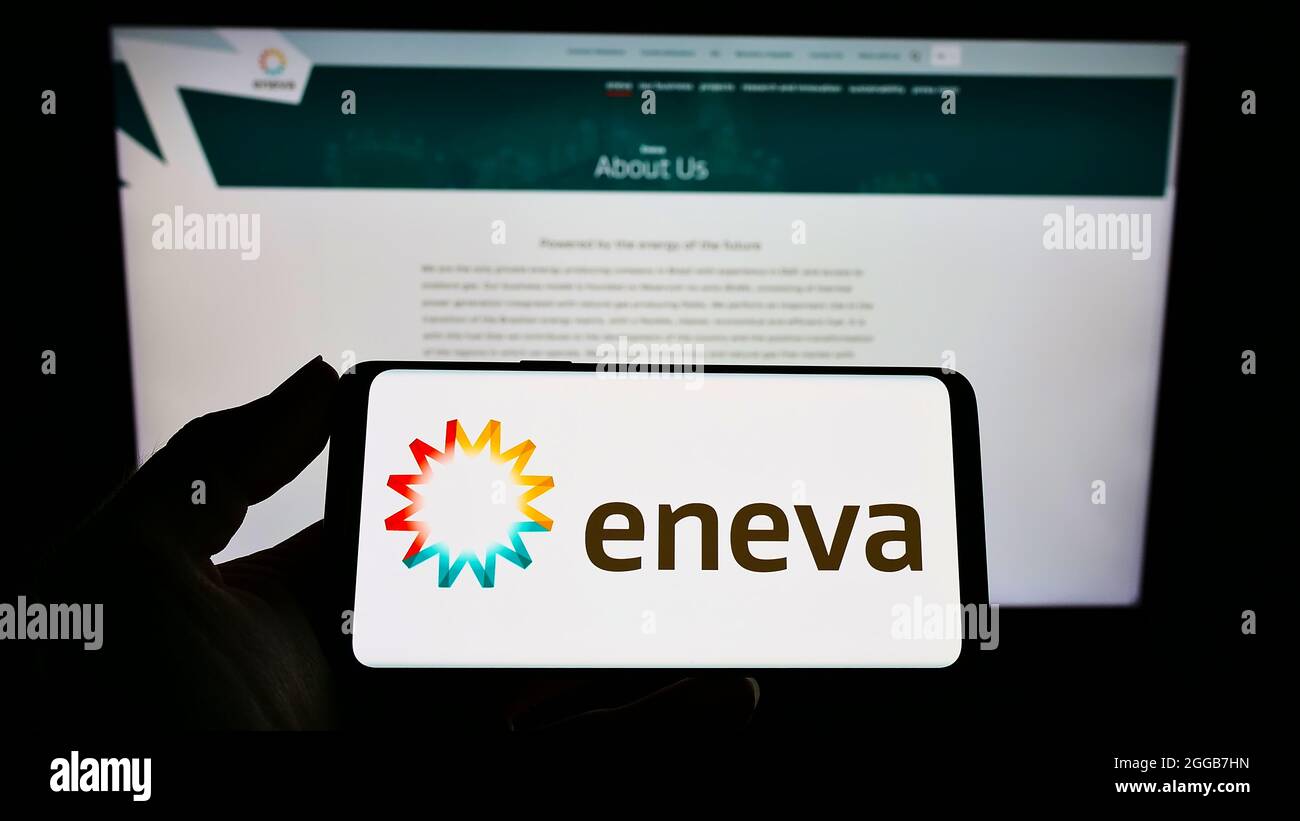 Persona che tiene uno smartphone con il logo della società brasiliana di produzione di energia ENEVA S.A. sullo schermo di fronte al sito web. Mettere a fuoco sul display del telefono. Foto Stock