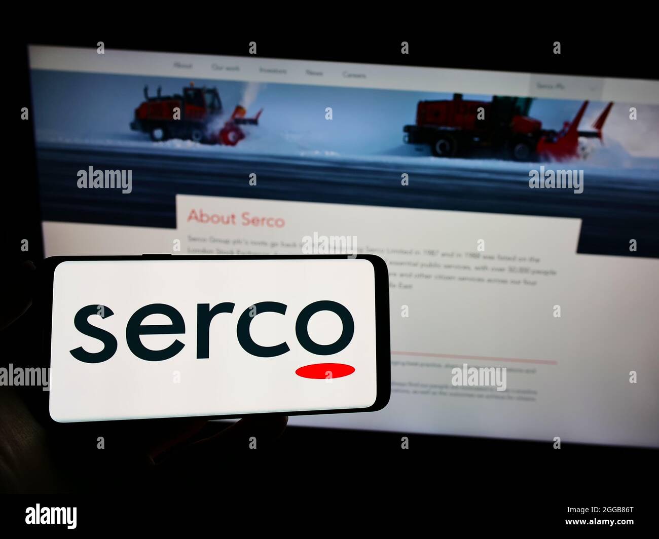 Persona che tiene il cellulare con il logo della società di servizi britannica Serco Group plc sullo schermo di fronte al sito web aziendale. Mettere a fuoco sul display del telefono. Foto Stock