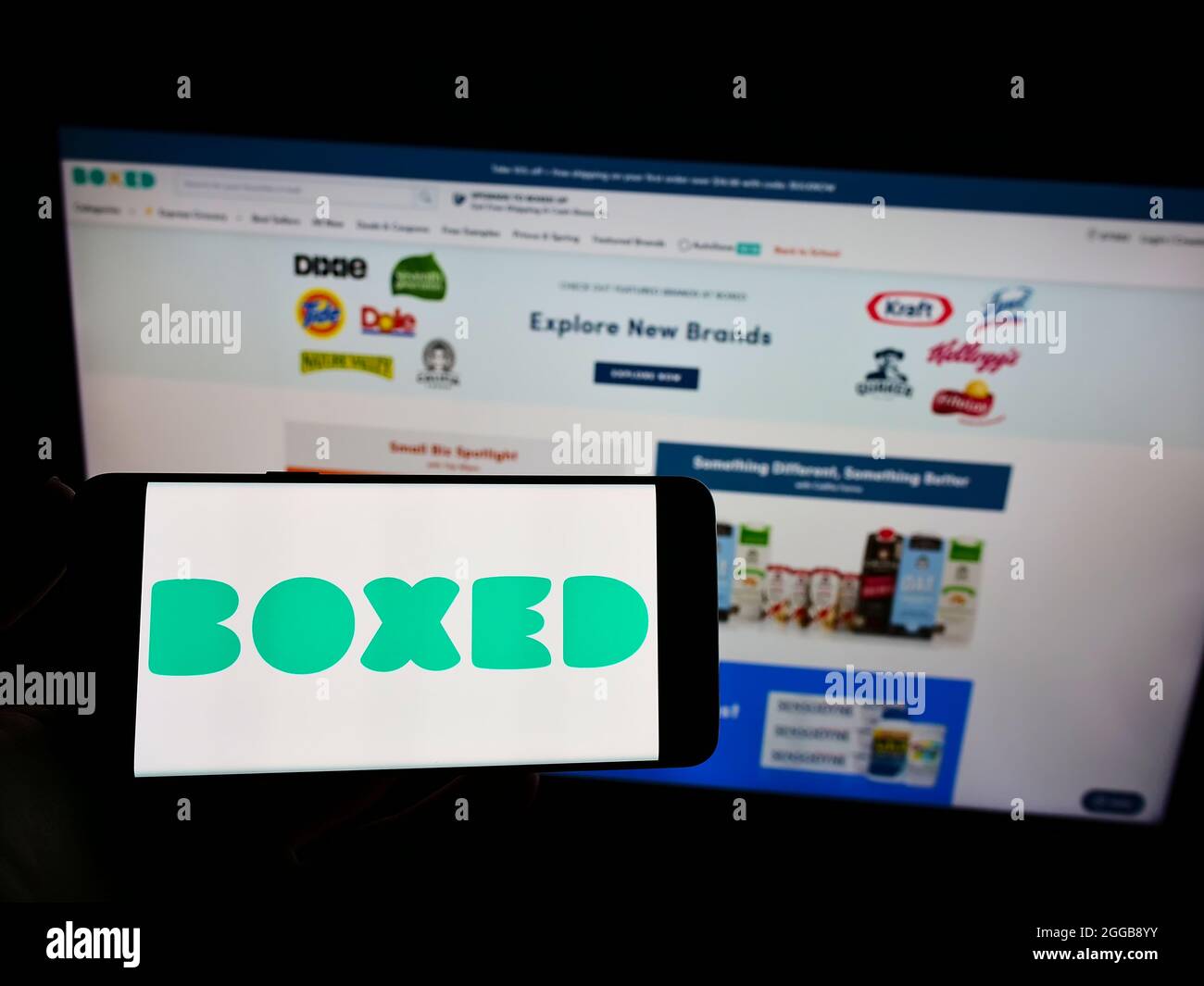 Persona che tiene il cellulare con il logo della società americana di vendita al dettaglio Giddy Inc. (Boxed.com) sullo schermo di fronte al sito web. Mettere a fuoco sul display del telefono. Foto Stock
