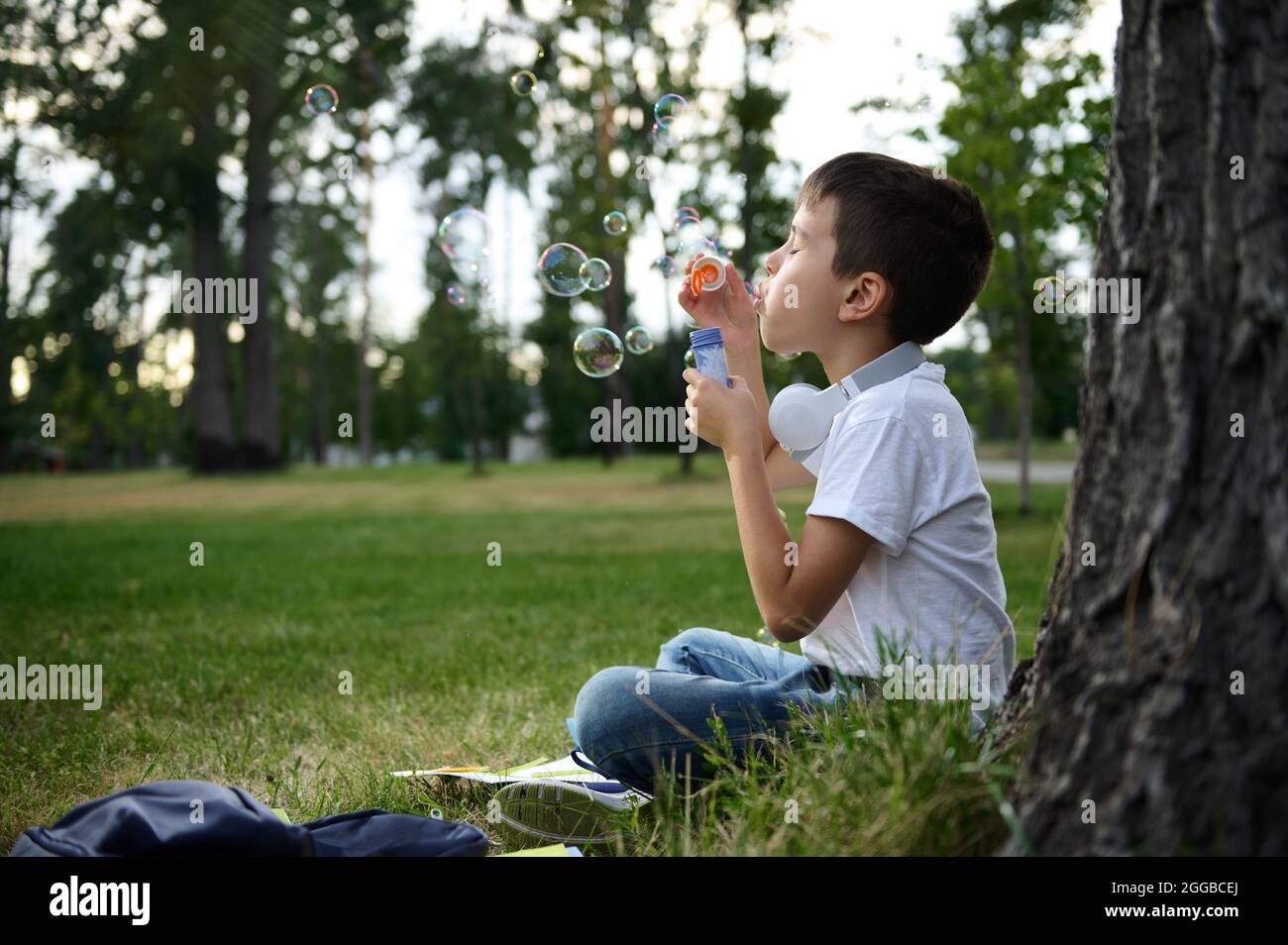 Ritratto di adorabile allegro bello carino ragazzo di scuola elementare invecchiato godendo la sua ricreazione tra le classi, soffiando bolle di sapone, seduto sul Foto Stock