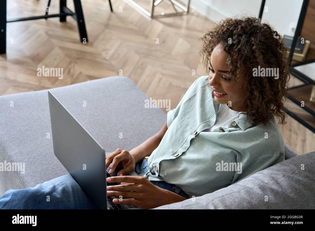Giovane afro americano donna blogger seduto sul divano a casa digitando sul portatile. Foto Stock