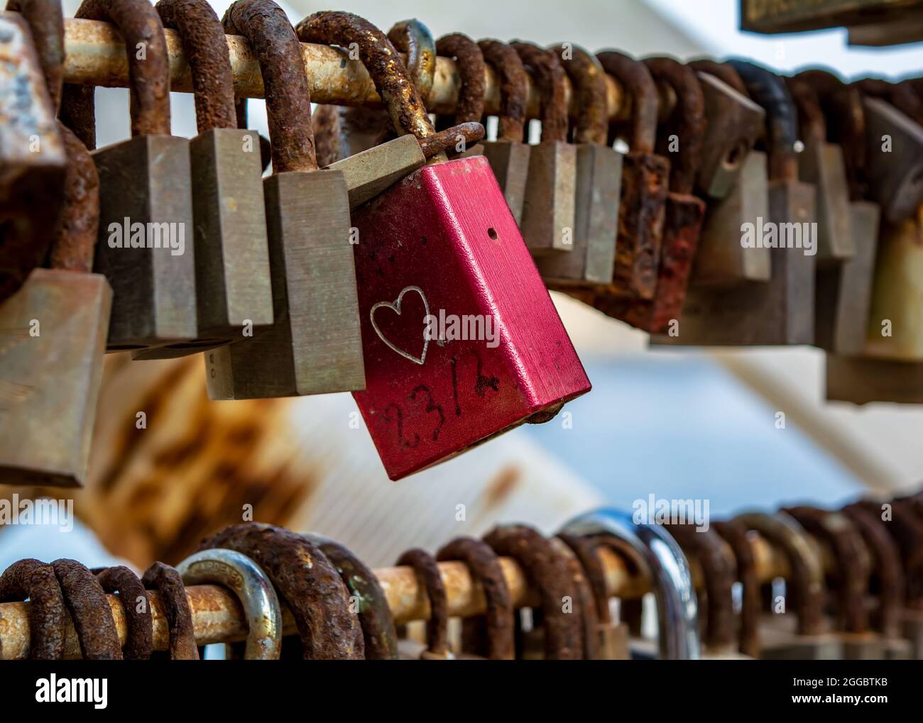 Rosso lucchetto d'amore con disegno cuore, appeso sul ponte tra le altre serrature arrugginite. Foto Stock