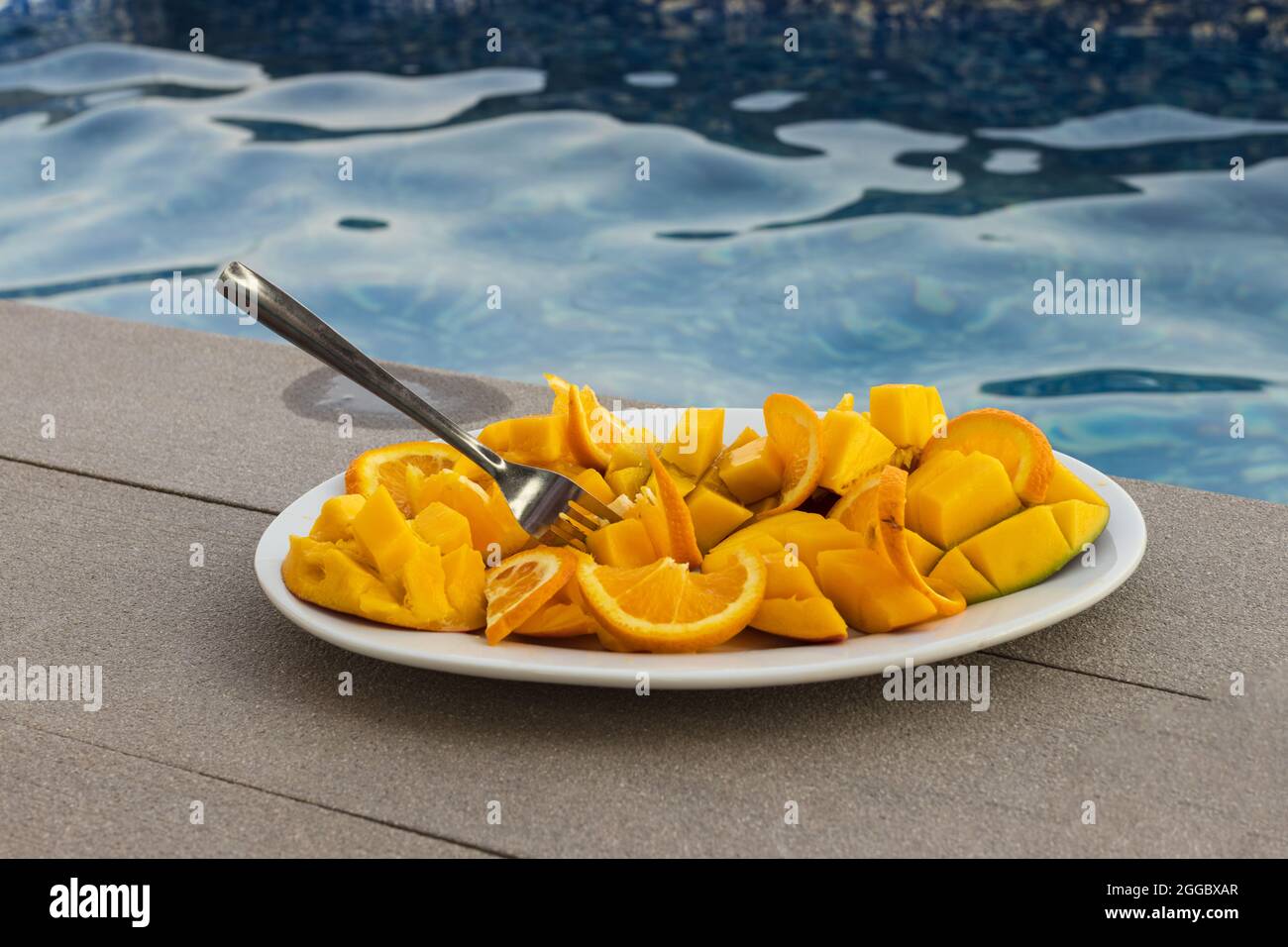 Fette di agrumi sul piatto grande su contro Blue pool acqua background.Orange per la dieta tropicale fresca Foto Stock