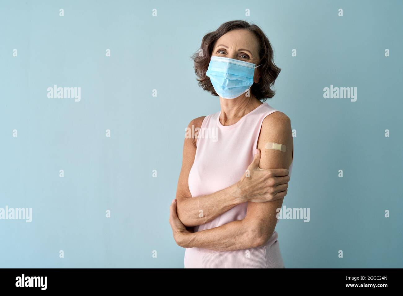 Ritratto di vecchia signora in maschera viso dopo vaccino covid con gesso sulla spalla. Foto Stock