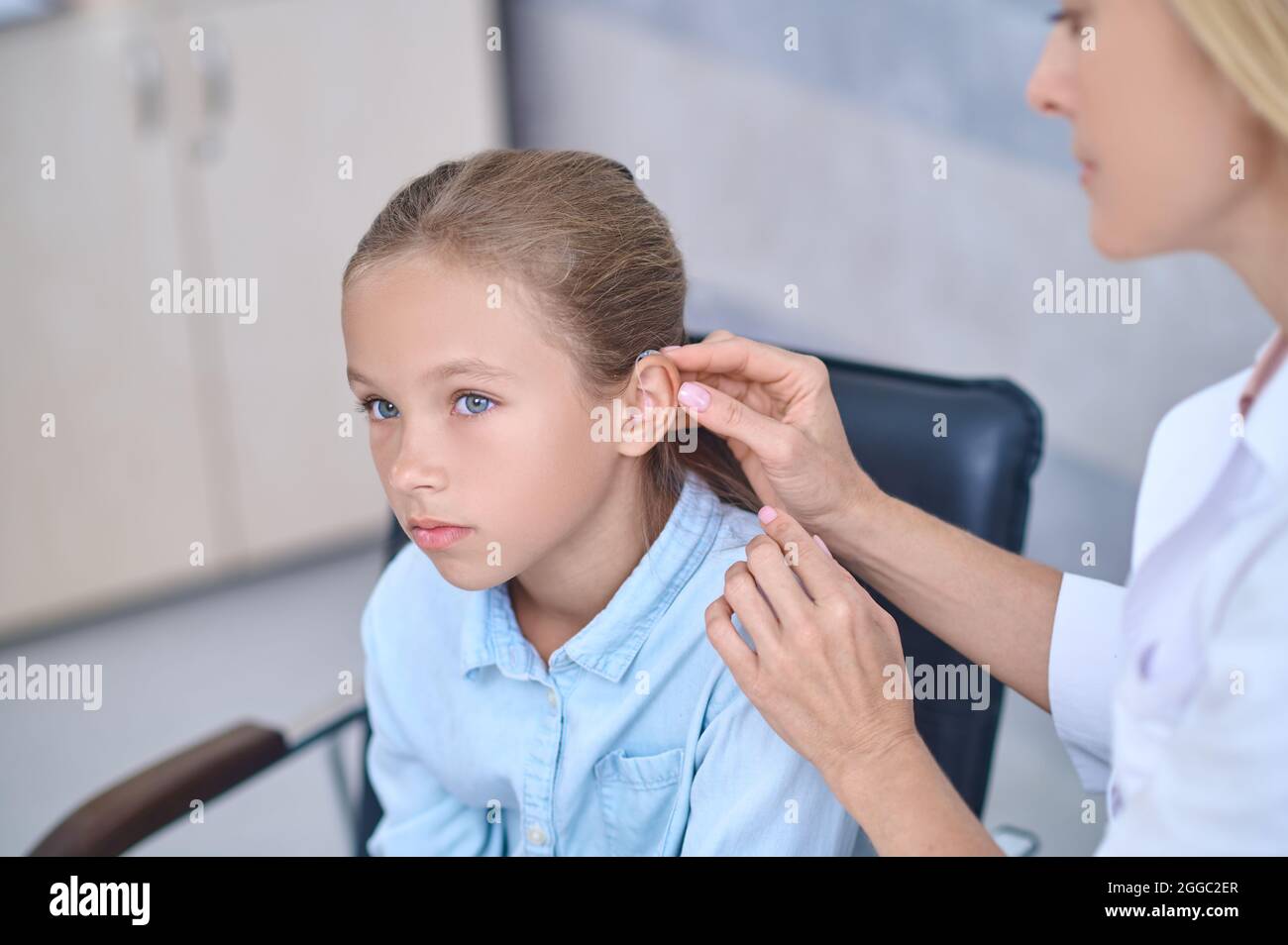 Medico qualificato che fissa un aiuto sordo dietro l'orecchio delle ragazze Foto Stock