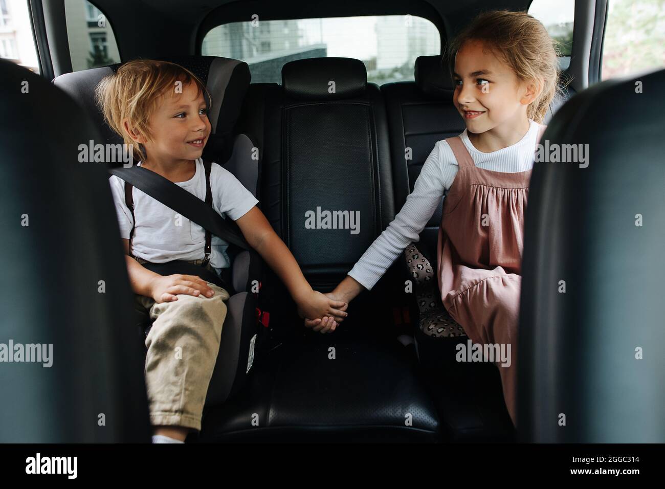 Due fratelli amorevoli seduti su un sedile posteriore di un'auto, tenendo le mani, guardandosi l'un l'altro. Mostrare il supporto. Foto Stock