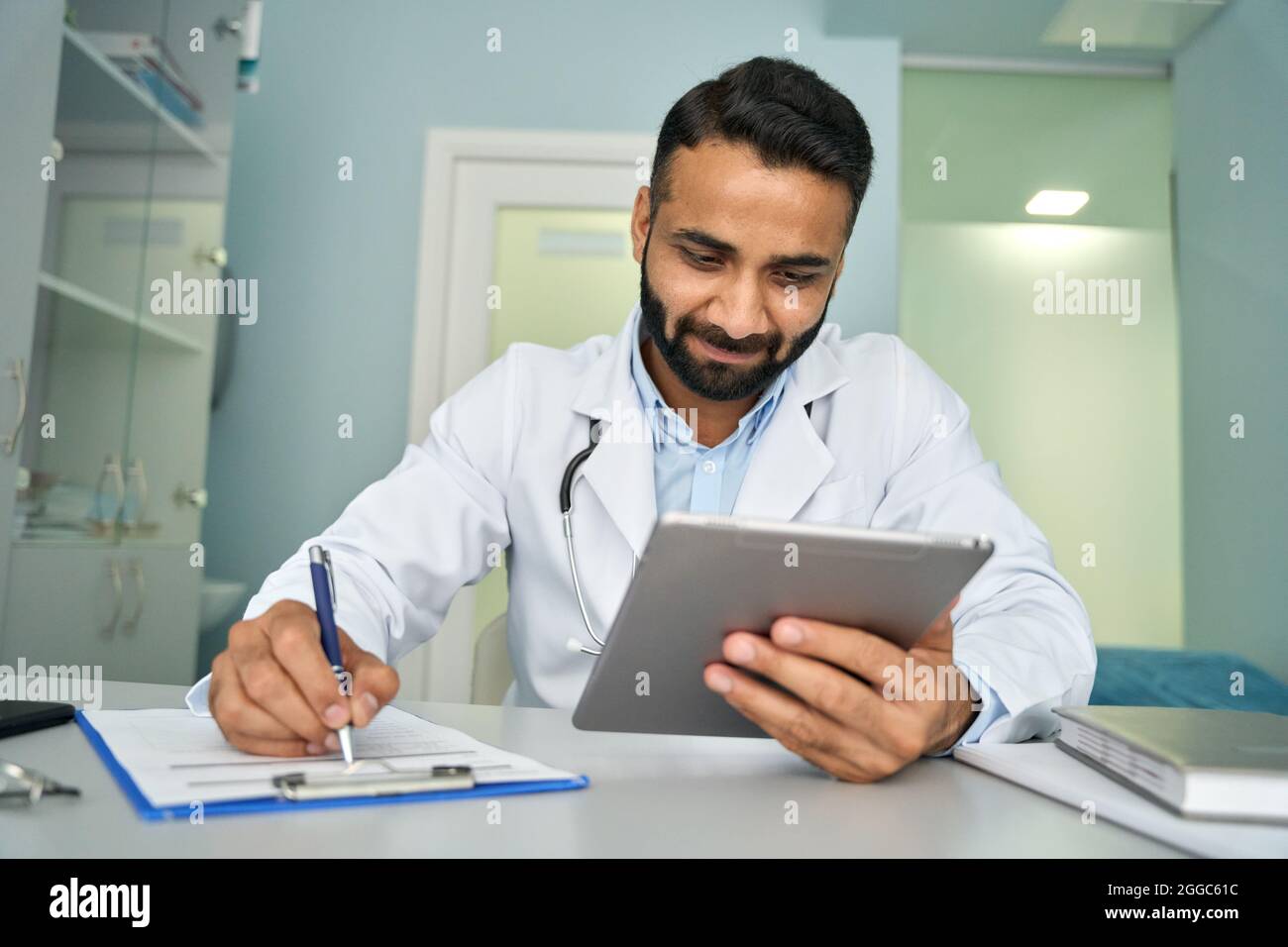 Medico indiano Happy maschile in clinica utilizzando tablet dispositivo di scrittura dati sanitari. Foto Stock